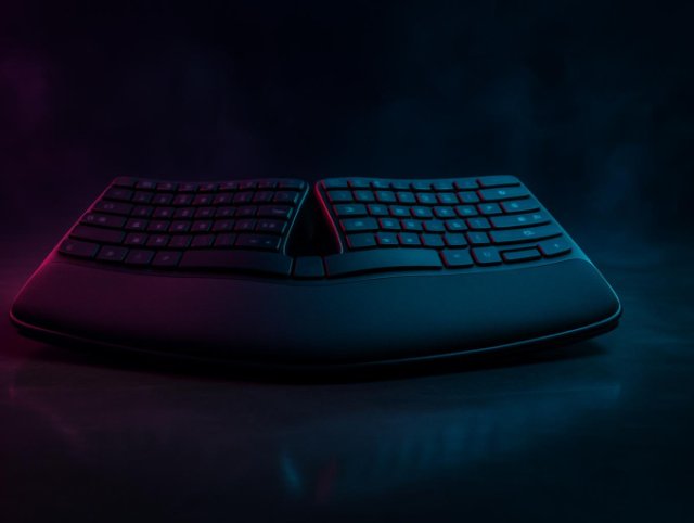 A split ergonomic keyboard with a curved wave layout and cushioned palm rest, lit by pink and cyan neon in a dark studio